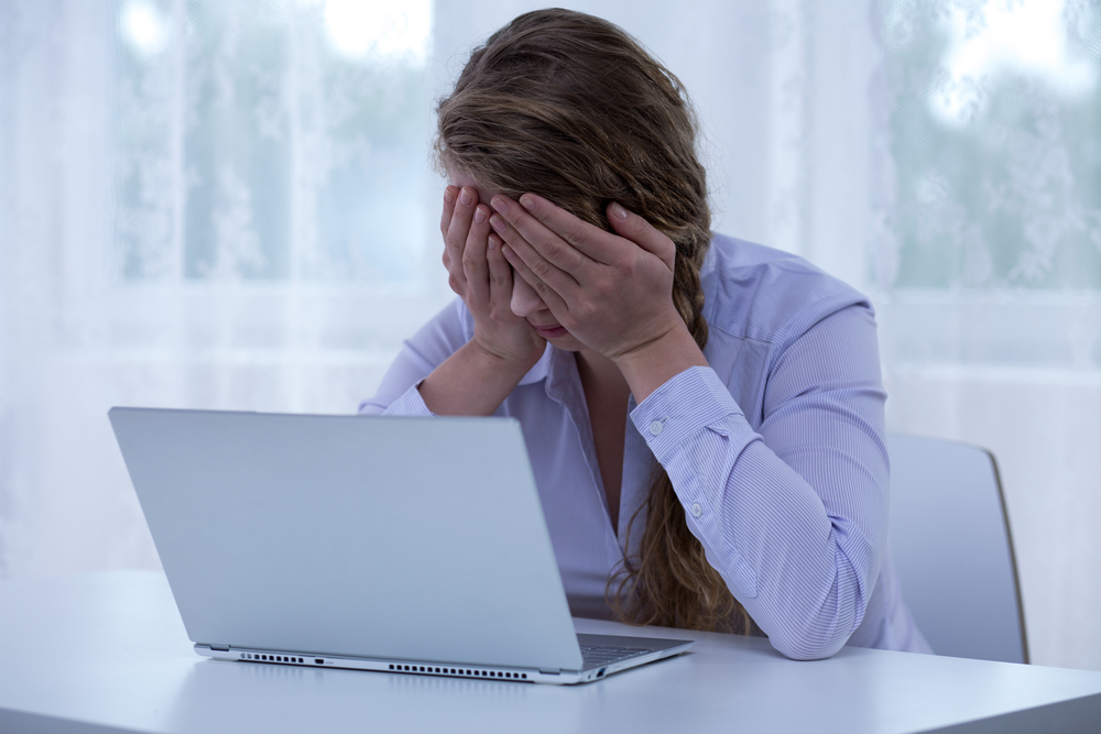 Woman with her head in her hands in front of a laptop.