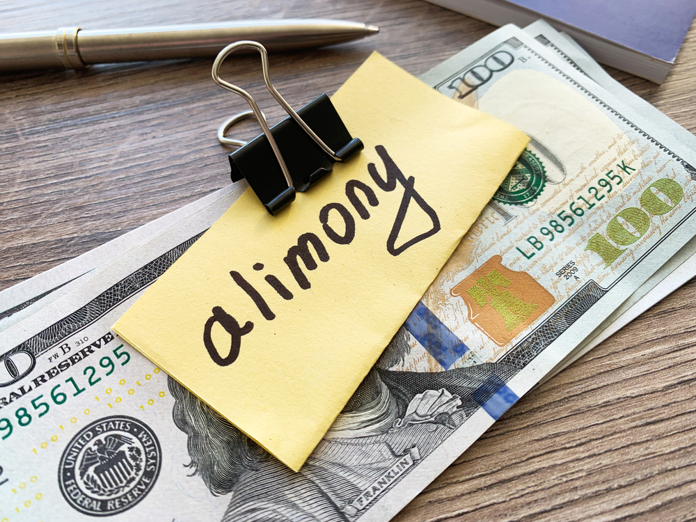 Stack of money clipped with paper labeled alimony