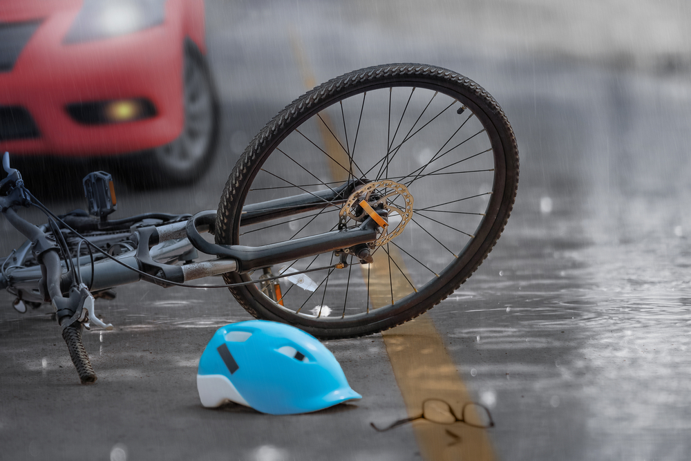 Bike and helmet laying on wet road in front of red car
