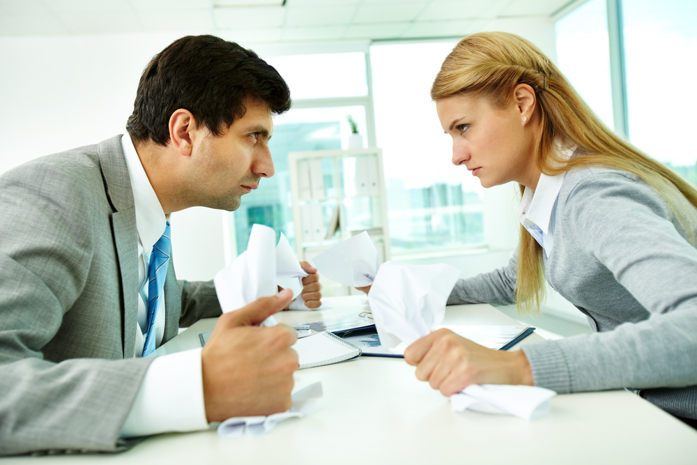 Man and woman in business attire glaring at each other across table