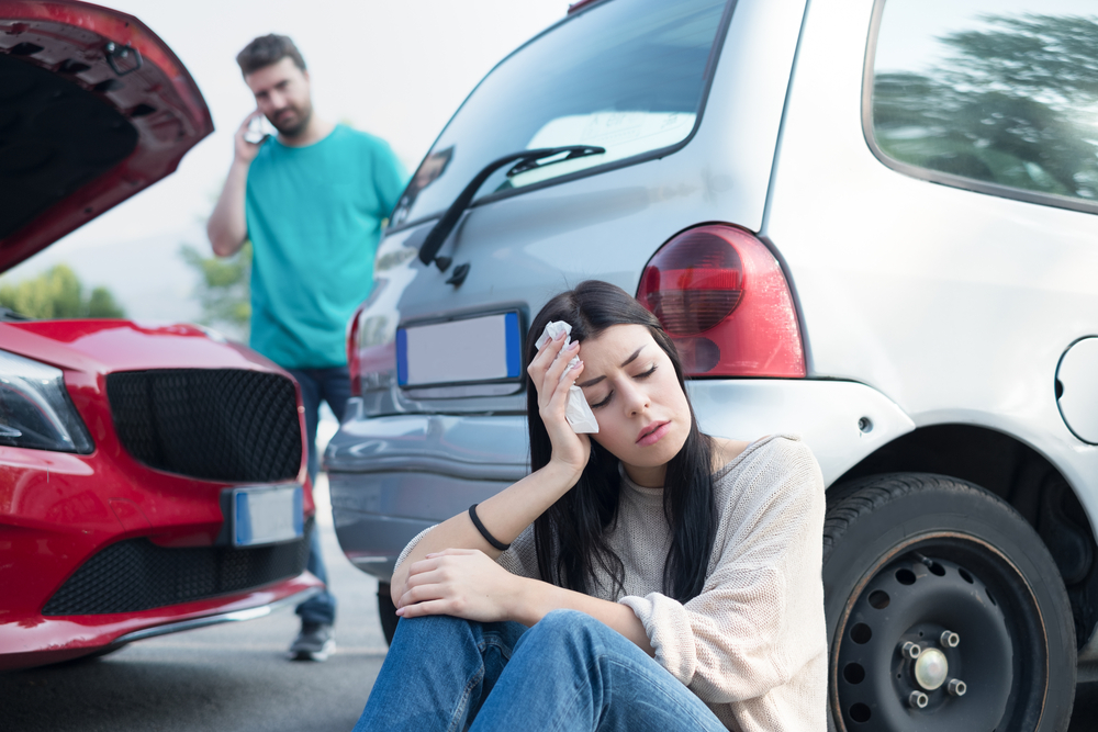 Injured woman sitting at car accident scene