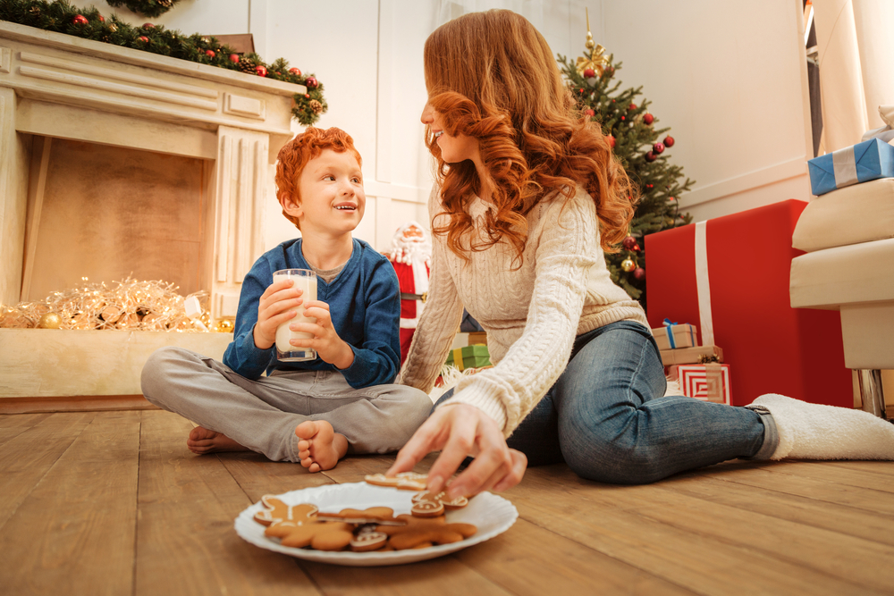 Mother and son sitting on floor and eating gingerbread cookies at Christmas time