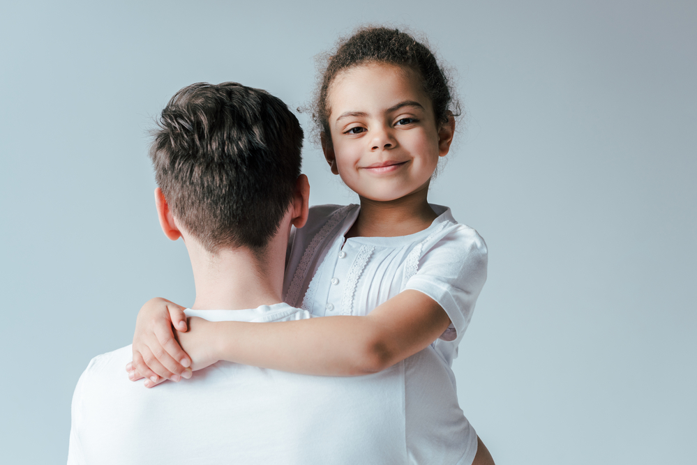 Girl hugging father and looking over his shoulder at camera