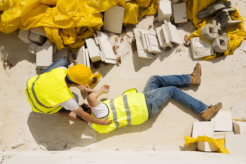 Construction worker trying to help injured worker lying on the ground