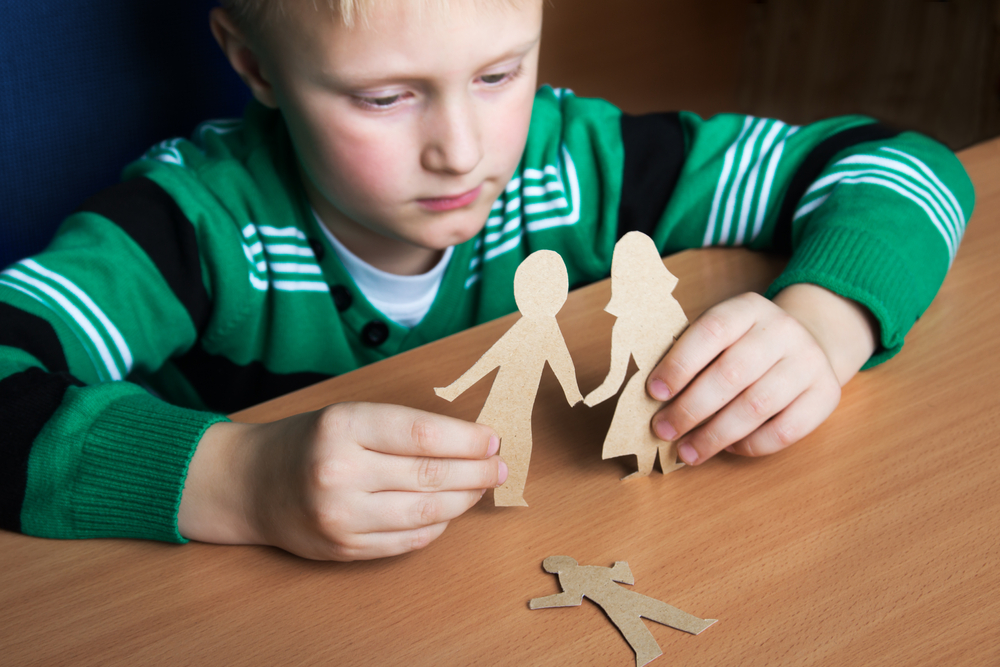 Sad little boy holding broken paper cutout of a family