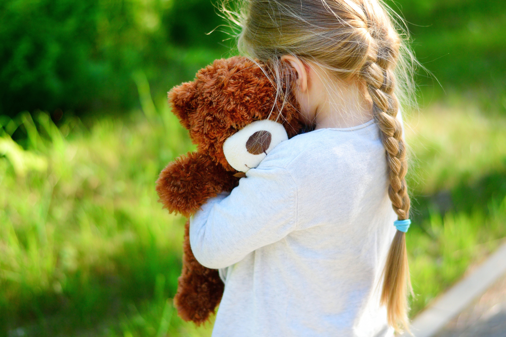 Sad girl facing away from camera and hugging teddy bear