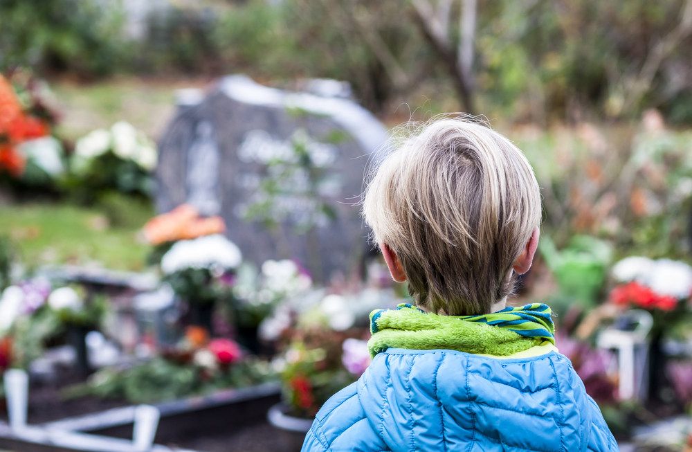 Back view of young boy standing in front of grave with flowers