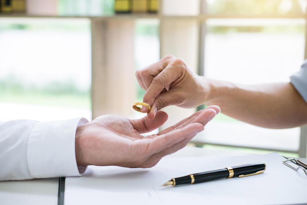 Woman placing wedding ring in man's hand, divorce papers underneath