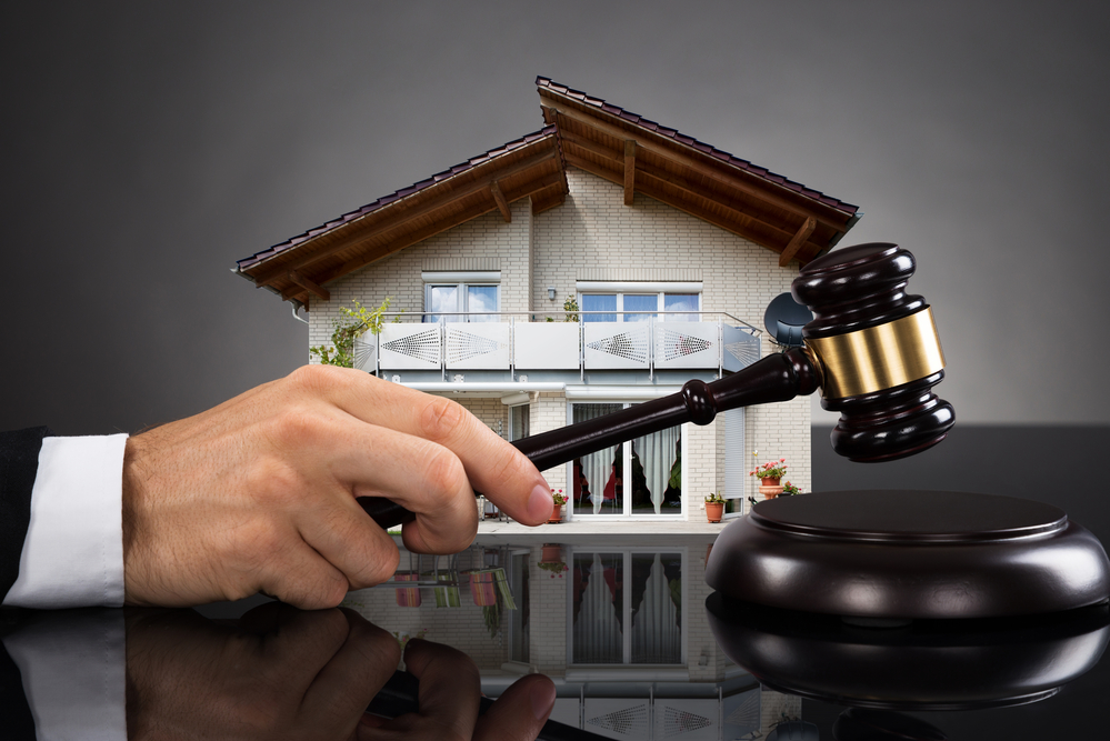 Hand holding gavel near model of house