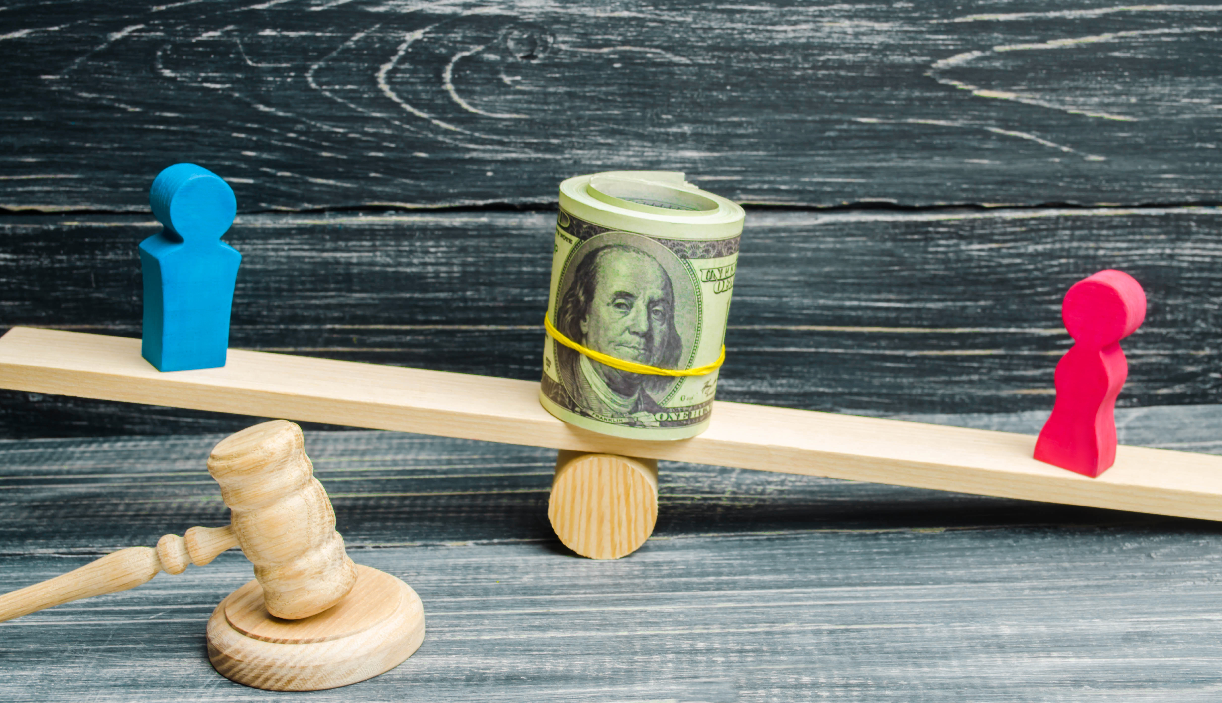 Red and blue figurines on scales with money in between