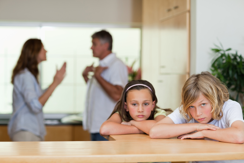 Upset children with parents fighting in background