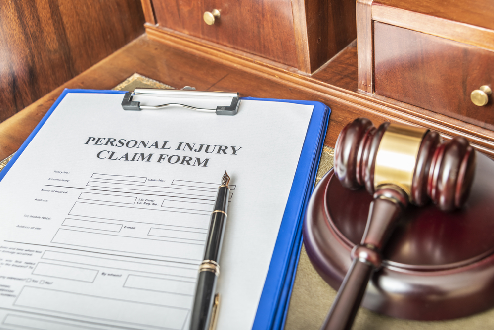 Personal injury claim form on clipboard with pen beside judge's gavel