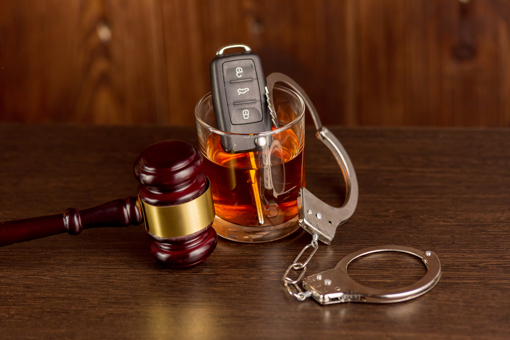 Glass of whiskey with car key, handcuffs, and judge gavel