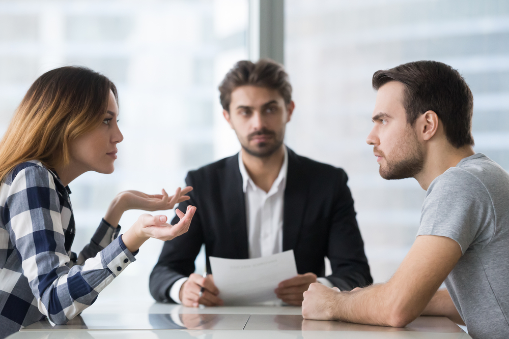 Young couple arguing at table in front of mediator