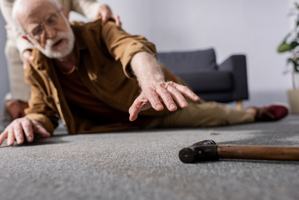 Fallen senior man reaching for nearby cane