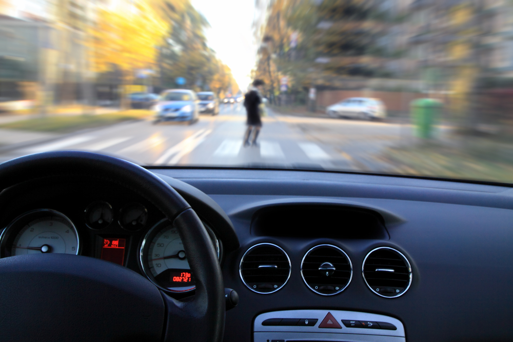 Pedestrian crossing street seen through windshield of approaching car