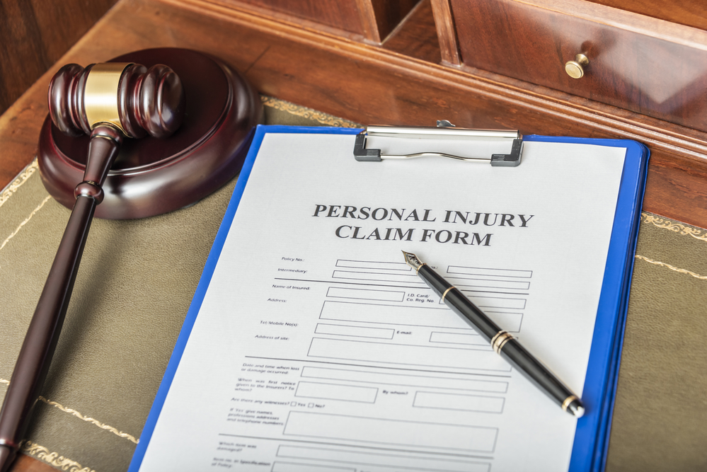 Personal injury claim form on blue clipboard next to gavel and pen