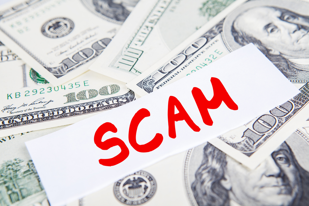Scam written in red on top of pile of money