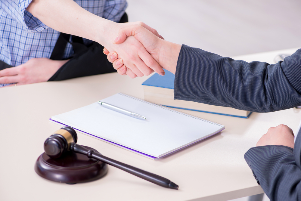 Close up of woman in sling shaking hands with attorney, with gavel in foreground