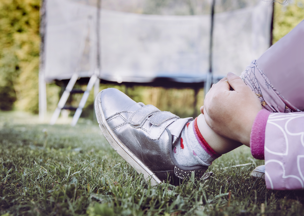 Child holding injured ankle with trampoline in background