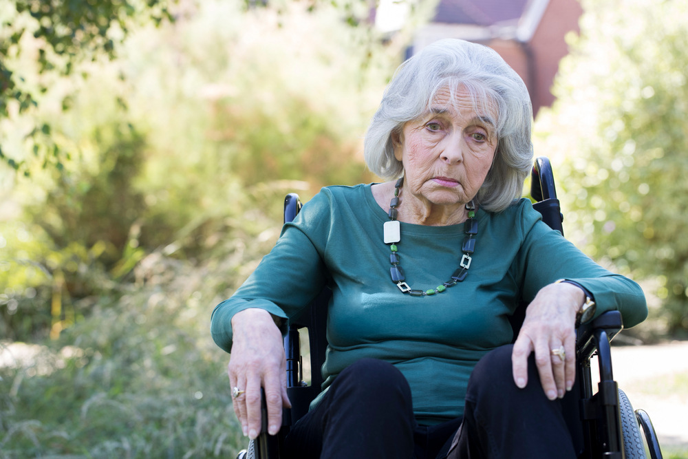 Depressed elderly woman sitting in wheelchair outdoors