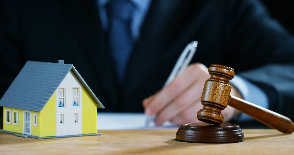 Man writing on paper near judge's gavel and model house