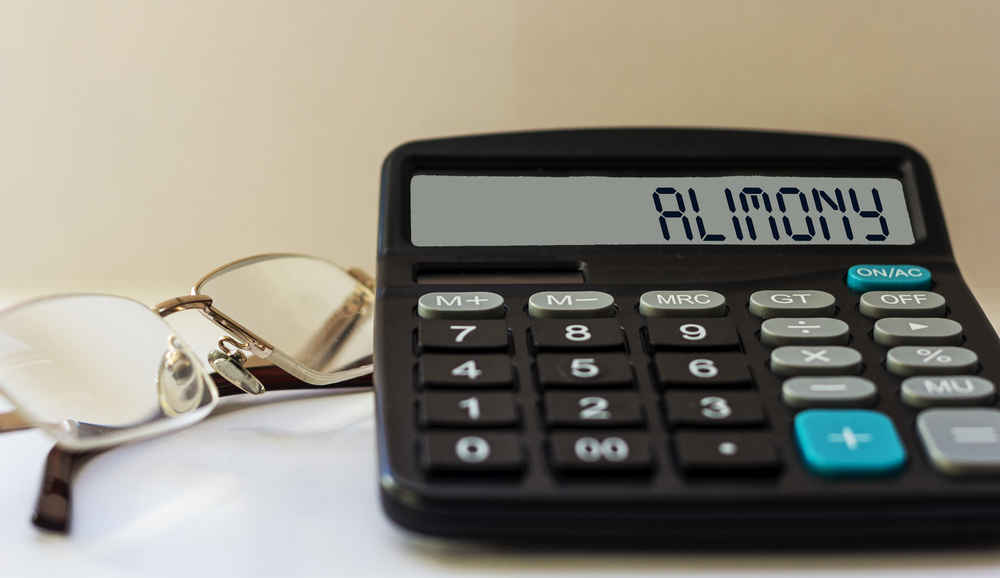 Pair of glasses on table next to calculator that says "Alimony" on screen