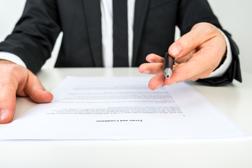 Businessman holding out pen with contract on table in front of him