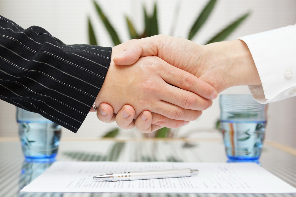 Close up of people shaking hands above paper and pen