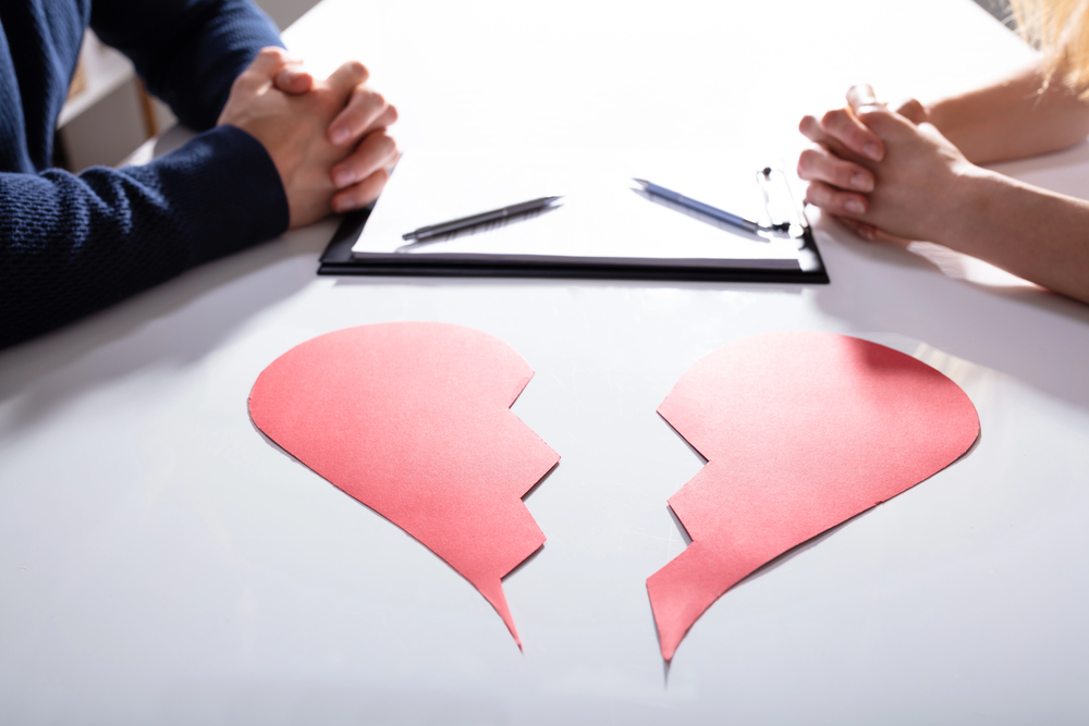 Broken paper heart on table in front of man and woman sitting opposite each other