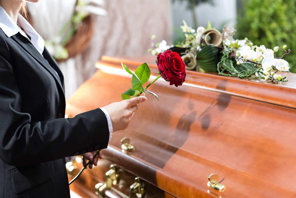Woman placing red rose on a casket